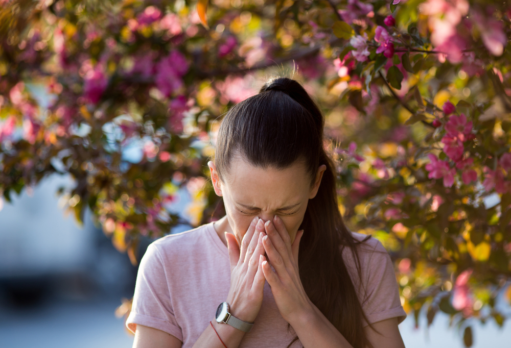 Young,pretty,woman,sneezing,in,front,of,blooming,tree.,spring