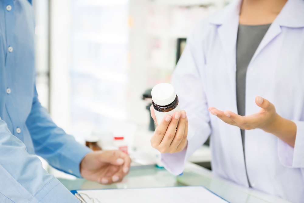 Female,pharmacist,holding,medicine,bottle,giving,advice,to,customer,in